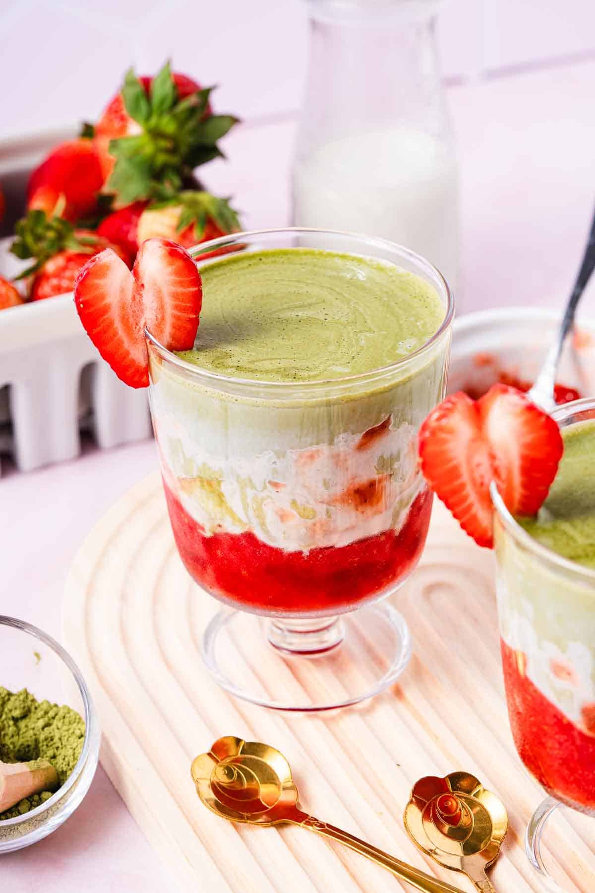 Layered Strawberry Matcha parfait in a glass, garnished with a sliced strawberry on the rim&mdash;a deliciously refreshing Strawberry Matcha Recipe you'll love to try.