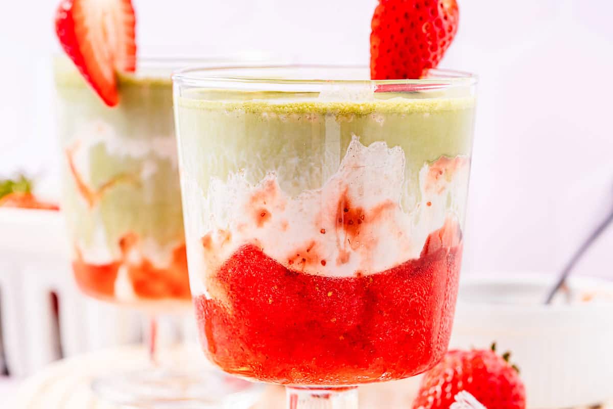 A layered strawberry and matcha parfait in a glass, topped with a sliced strawberry&mdash;a delightful Strawberry Matcha Recipe perfect for any occasion.