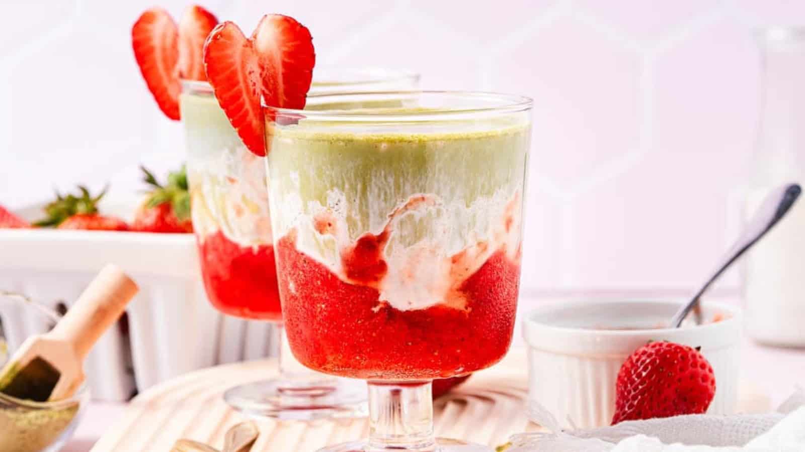 A layered strawberry and matcha dessert in a glass, garnished with a sliced strawberry on the rim.