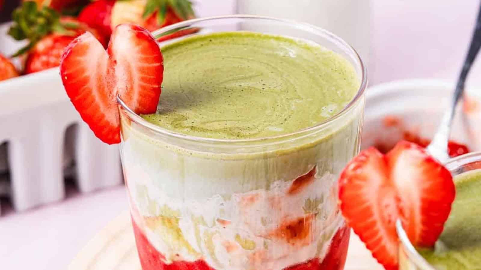 A layered strawberry and matcha dessert in a glass, garnished with a sliced strawberry on the rim.