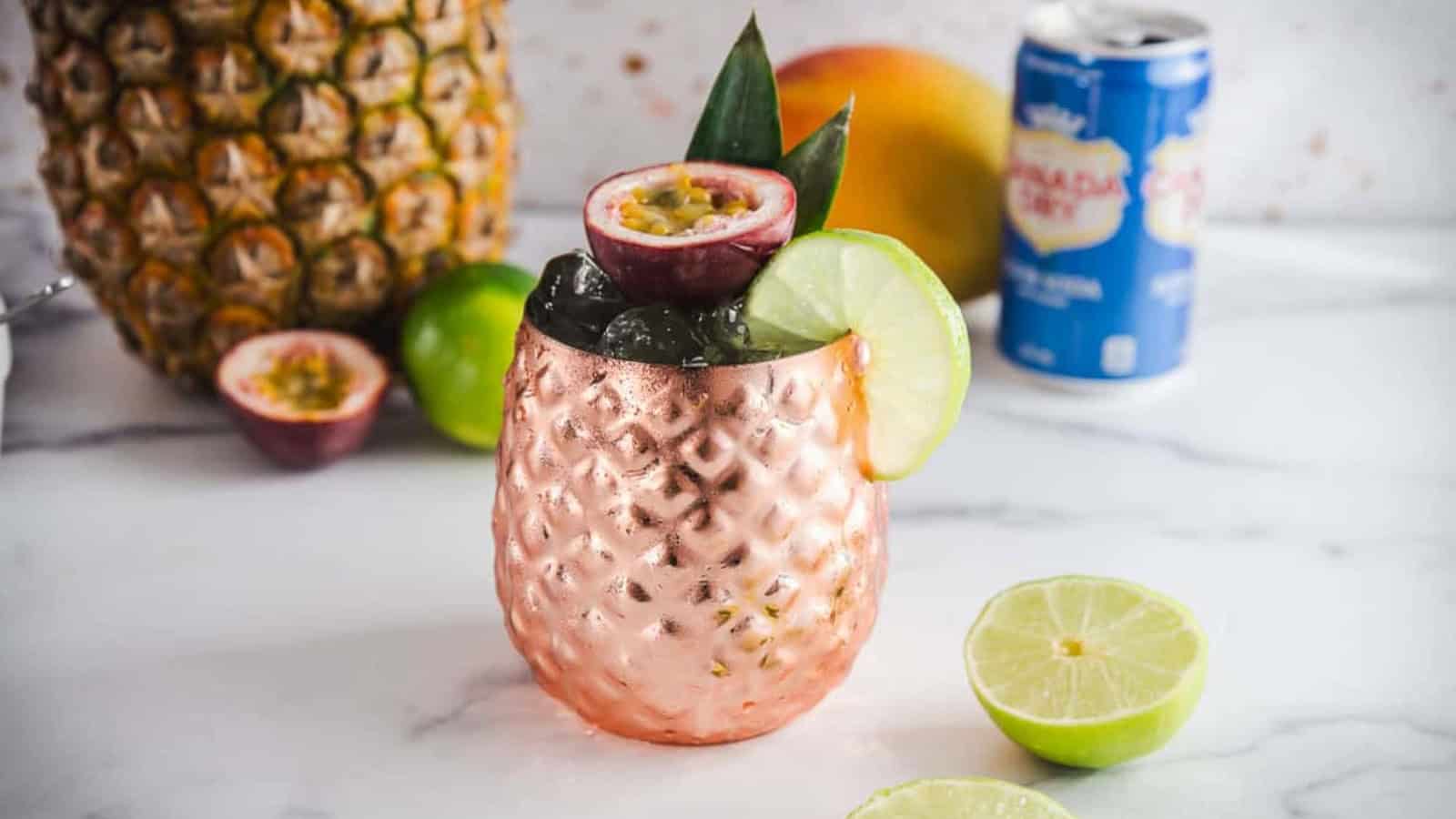 A tropical cocktail in a copper pineapple cup, garnished with lime, passionfruit, and pineapple leaves.