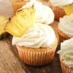 Cupcake with white frosting and a fresh pineapple slice on top, inspired by Dole Whip cupcakes, placed on a wooden surface.