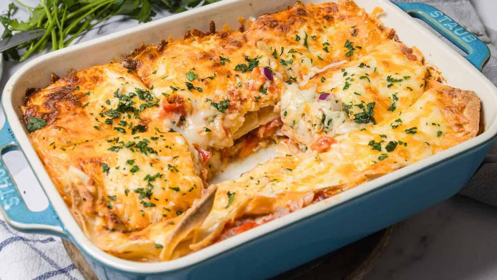A cheesy baked lasagna in a blue dish, garnished with herbs, with one slice missing.