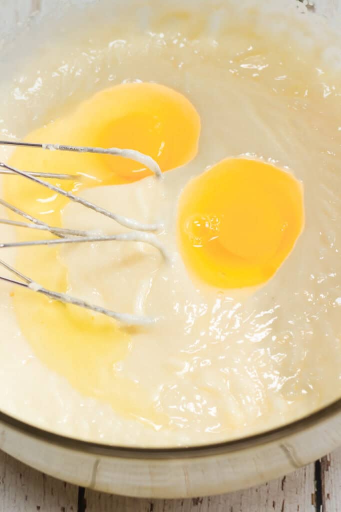 Two raw eggs and a whisk in a bowl of batter, ready to be mixed for delicious Amish lemon cookies.