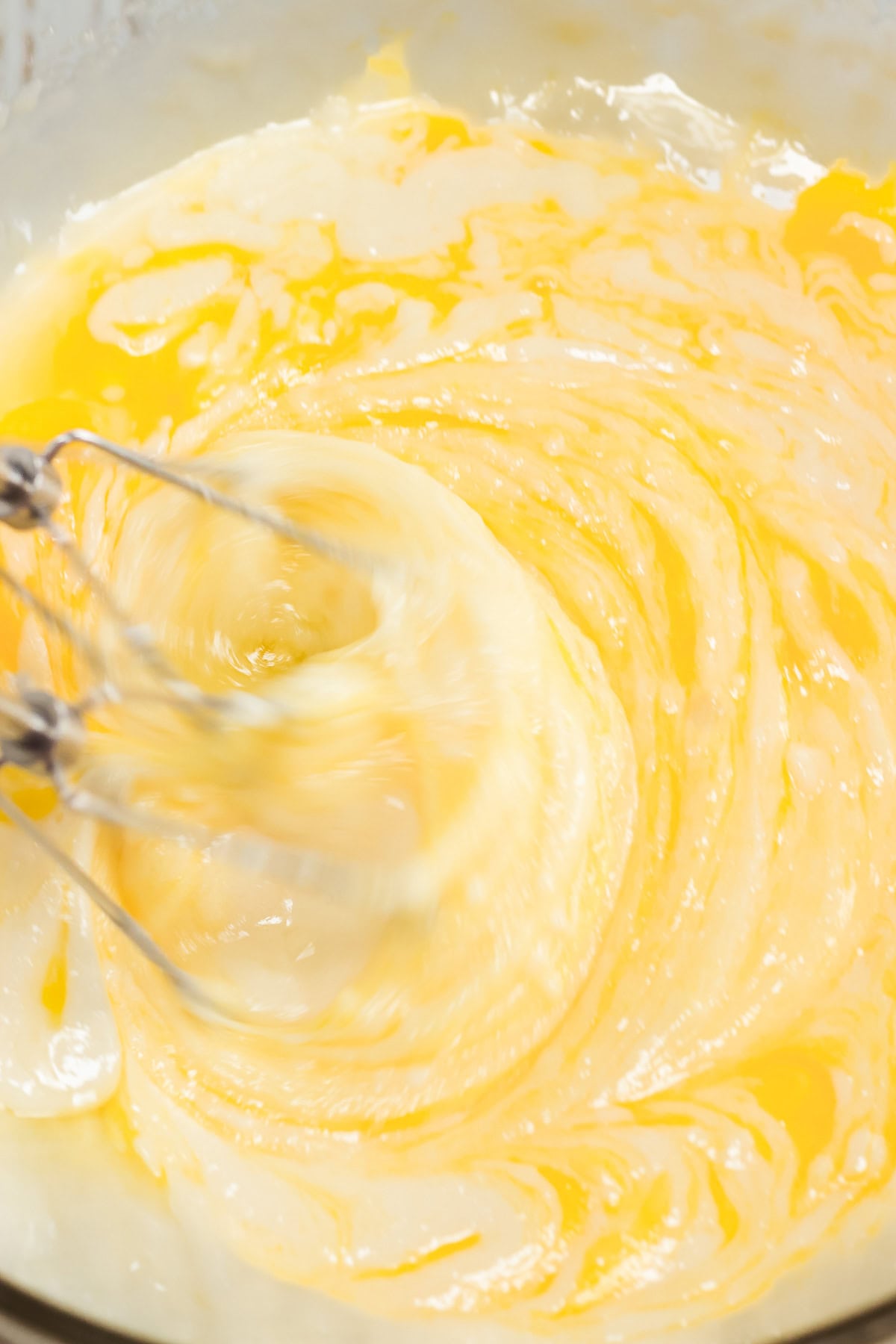 Electric beaters mixing yellow batter in a bowl, creating a swirling motion with creamy textures&mdash;the perfect start for classic Amish cookies or lemon sugar cookies.