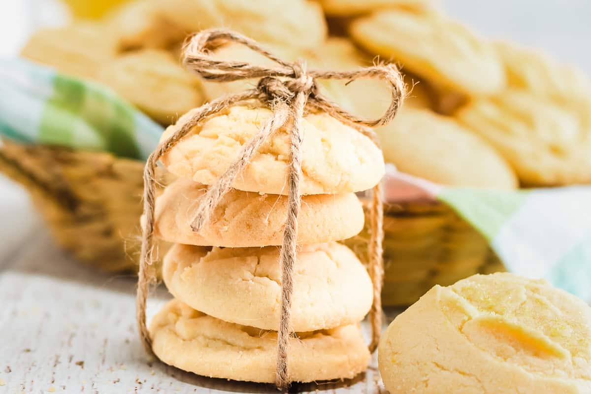 Four Amish lemon cookies are stacked and tied with twine, with more cookies in a basket in the background.