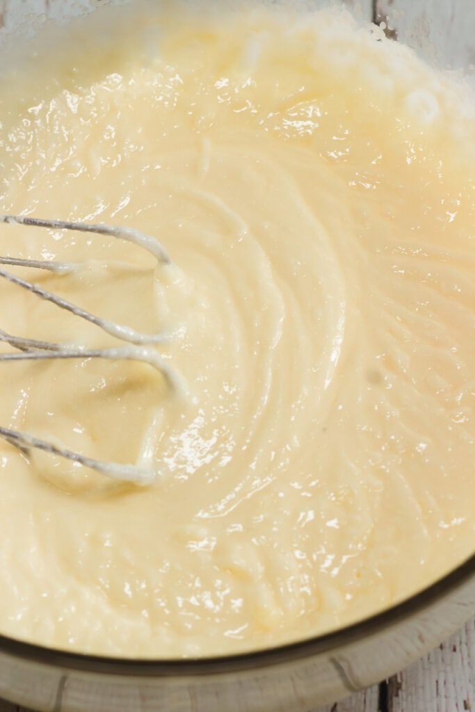 Electric beaters mixing creamy cake batter in a glass bowl on a light wooden surface, perfect for creating classic Amish cookies.