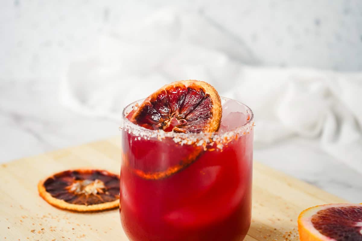 A glass of blood orange juice with ice, garnished with a dried orange slice and a salted rim&mdash;perfect for a refreshing margarita mocktail.