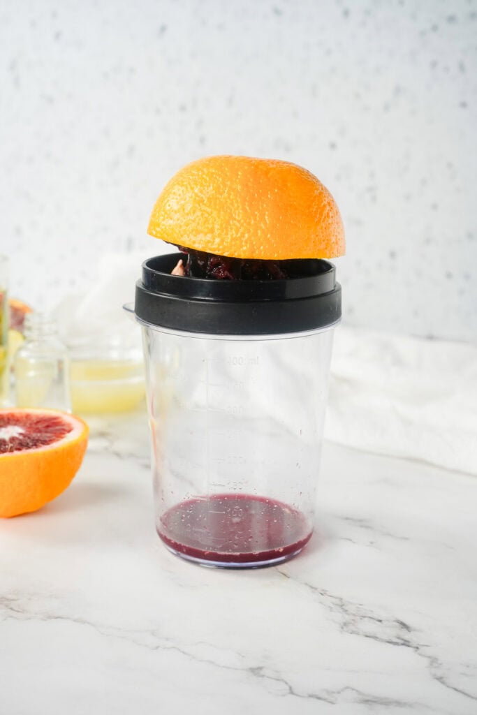 Half a blood orange placed on a juicer over a clear measuring cup with juice at the bottom, perfect for making a refreshing Margarita Mocktail.