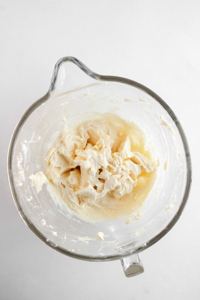 Glass mixing bowl with partially mixed butter and sugar on a white background, preparing the base for delicious Dole Whip Cupcakes.