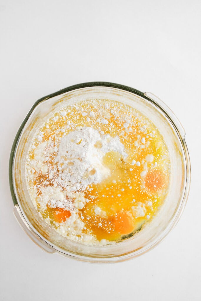A glass bowl with flour, eggs, and liquid ingredients ready to be mixed for delicious Dole Whip Cupcakes on a white background.