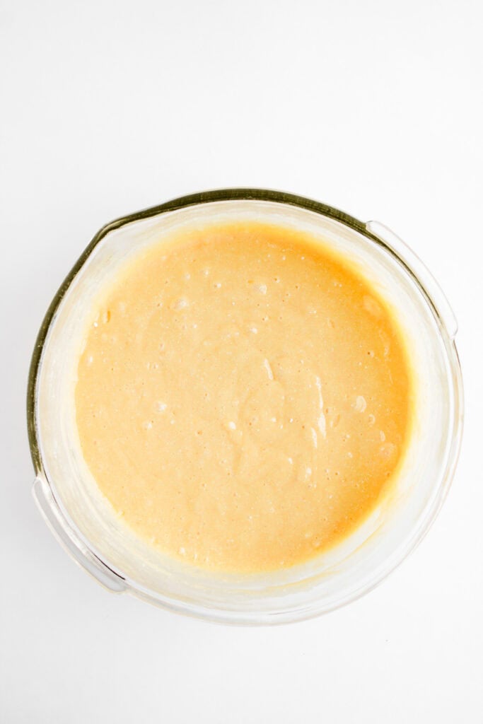 Glass bowl filled with smooth, lightly bubbly yellow cake batter for Dole Whip Cupcakes on a white background.