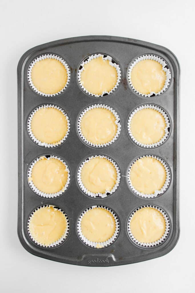 Muffin pan with 12 paper liners filled with raw yellow Dole Whip Cupcakes batter on a white background.