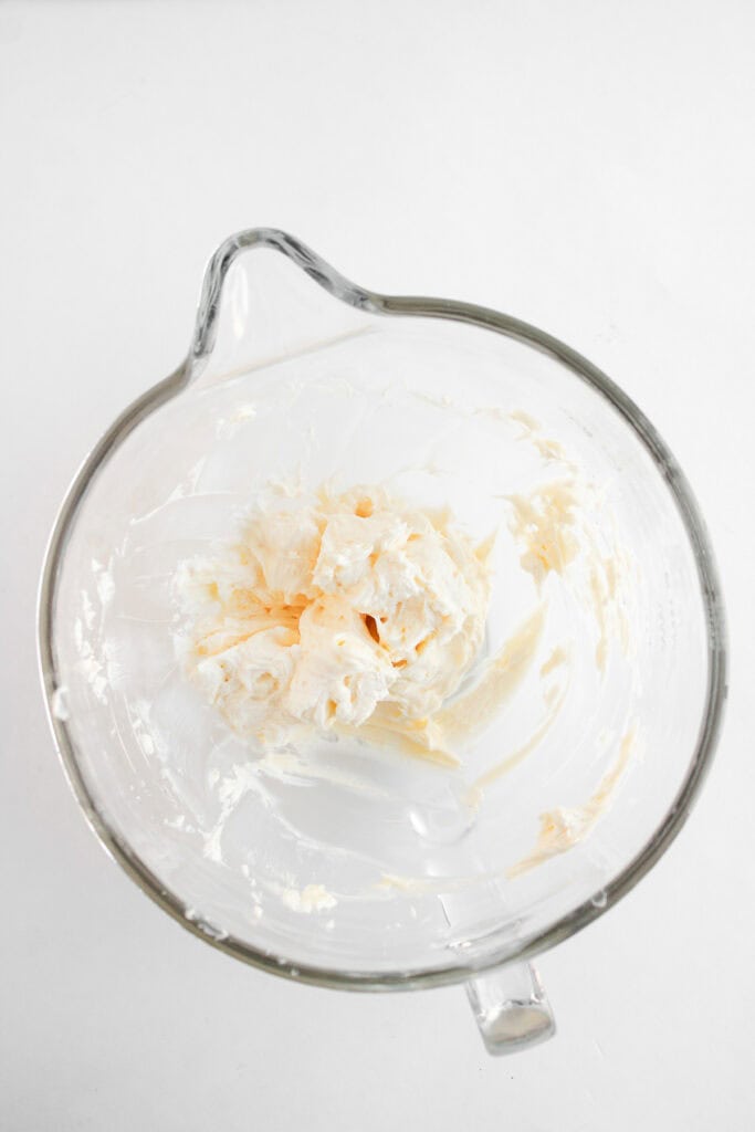 A glass mixing bowl with a dollop of whipped cream or frosting, perfect for topping your Dole Whip Cupcakes, against a white background.