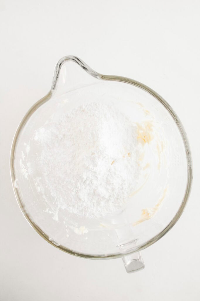 Glass mixing bowl with powdered sugar and traces of butter on a white surface, viewed from above&mdash;perfect for whipping up cupcakes or recreating that classic Dole Whip flavor at home.