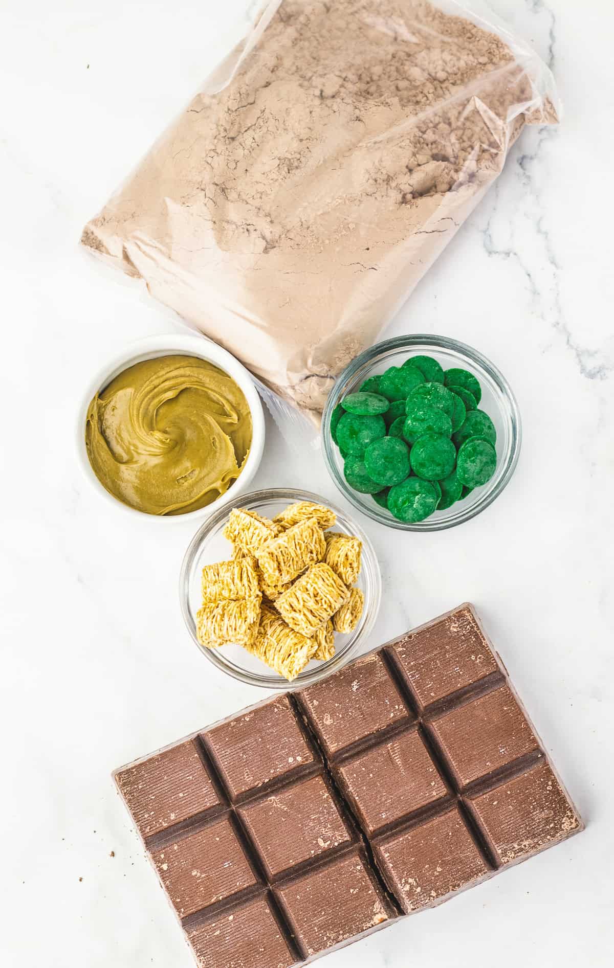 A bag of cocoa powder, green candy melts, peanut butter, shredded wheat squares, and a chocolate bar&mdash;perfect ingredients for trying out a Dubai Chocolate Brownie or your favorite chocolate brownie recipe.