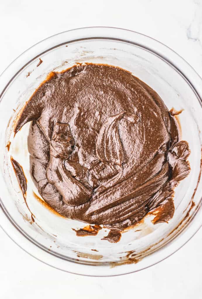 A glass bowl filled with thick, smooth chocolate brownie batter on a white surface, ready for baking with an authentic Dubai Brownie Recipe.