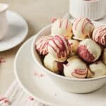 A bowl of Strawberry Cake Balls coated with white chocolate and drizzled with red icing, perfect for any sweet occasion.