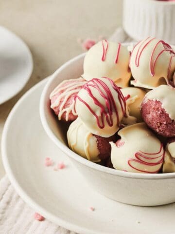 A bowl of Strawberry Cake Balls coated with white chocolate and drizzled with red icing, perfect for any sweet occasion.