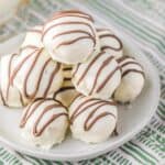 A plate of white chocolate Zebra Cake Balls, drizzled with milk chocolate, stacked on a striped green and white cloth.