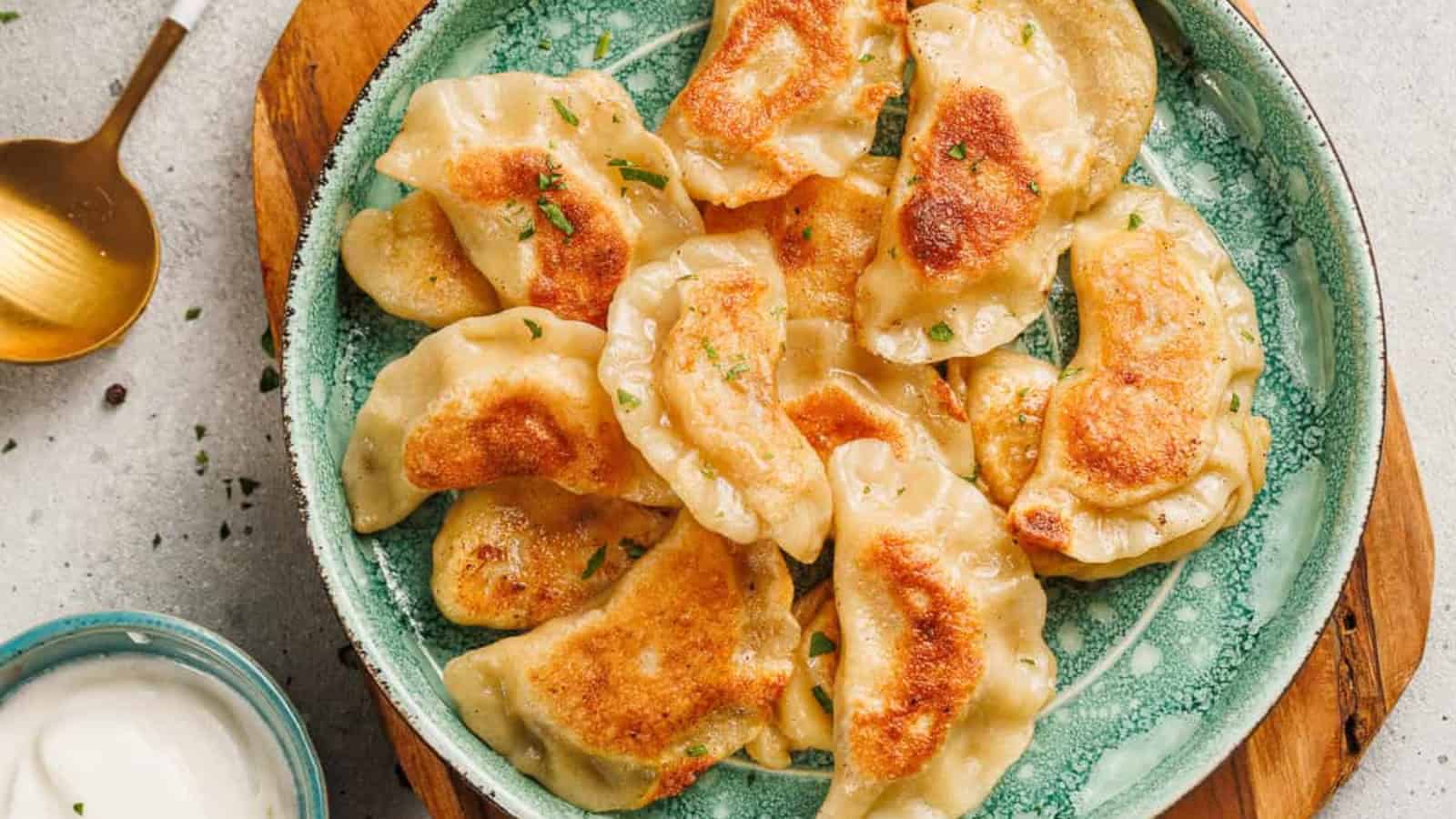 A plate of golden-brown fried dumplings garnished with herbs, next to a bowl of white dipping sauce.