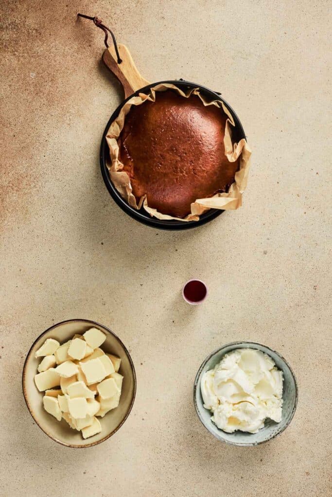 Round baked Strawberry Cake in a pan, with bowls of butter, cream cheese, and a small cup of red liquid nearby&mdash;perfect ingredients for your next Strawberry Cake Balls recipe.