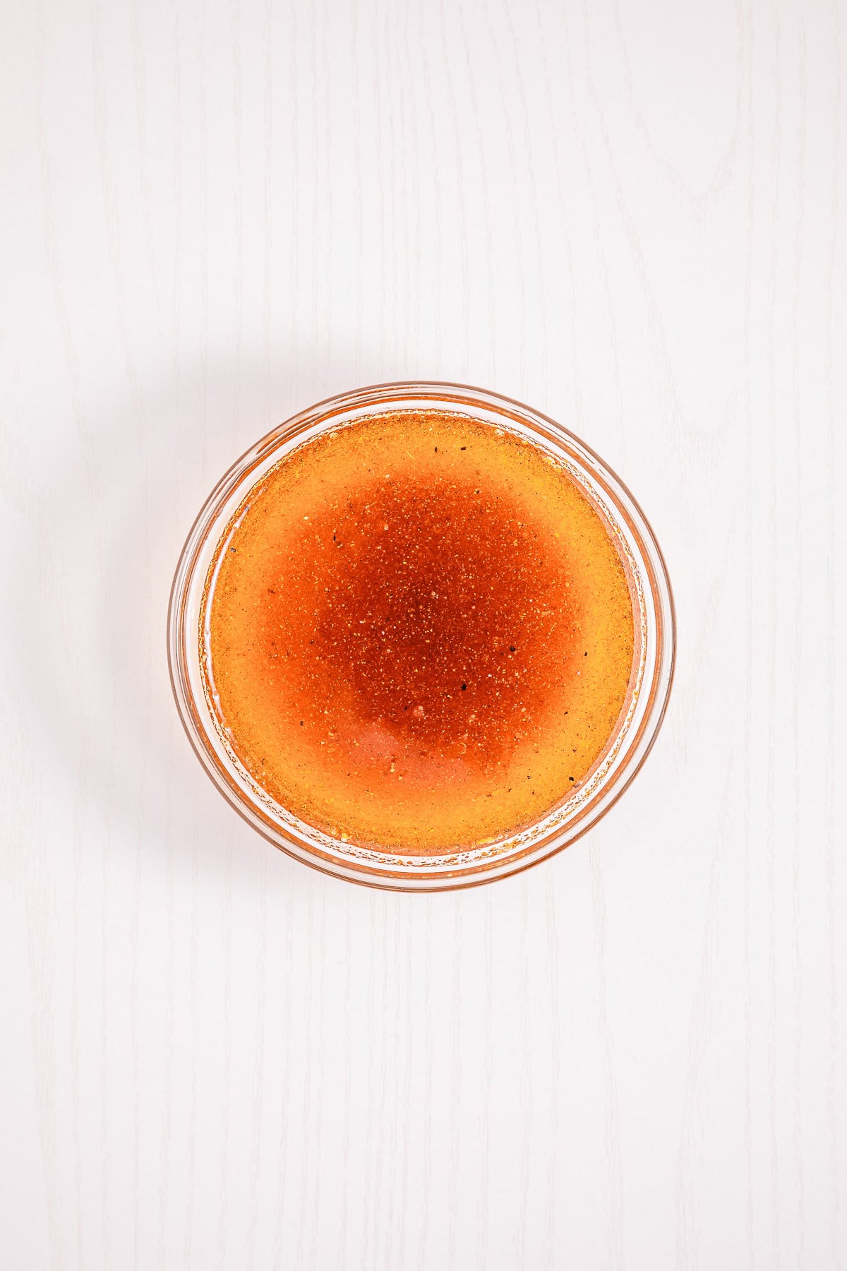 A round glass dish filled with caramelized cr&egrave;me br&ucirc;l&eacute;e on a light wooden surface, viewed from above&mdash;perfect alongside a serving of Cowboy Caviar for a delightful contrast of flavors.