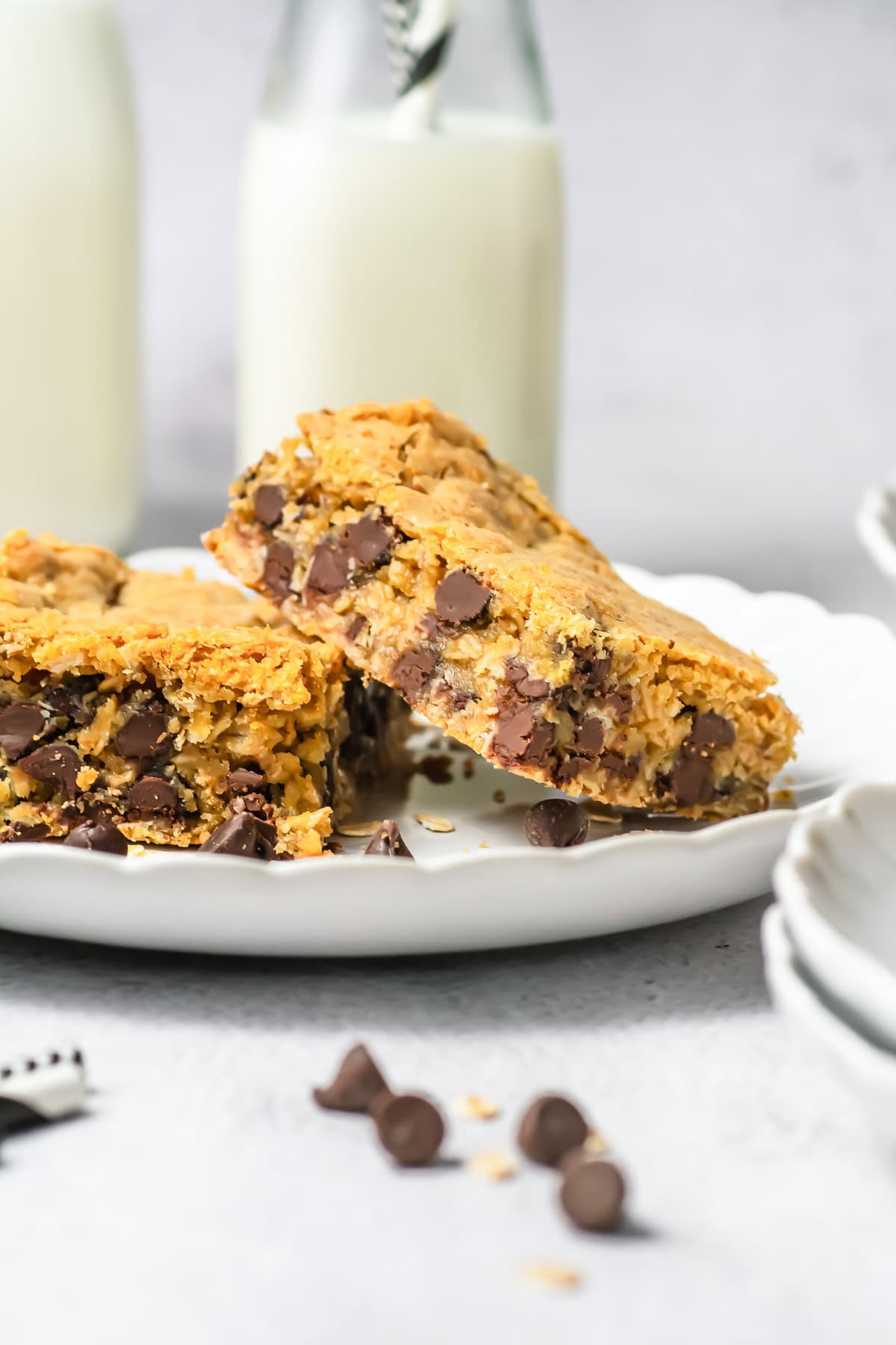Two chocolate chip oatmeal bars stacked on a plate with milk bottles in the background.
