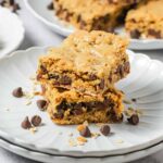Two chewy Oatmeal Bars stacked on a plate, with chocolate chips and oats scattered around.