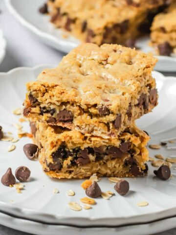 Two chewy Oatmeal Bars stacked on a plate, with chocolate chips and oats scattered around.