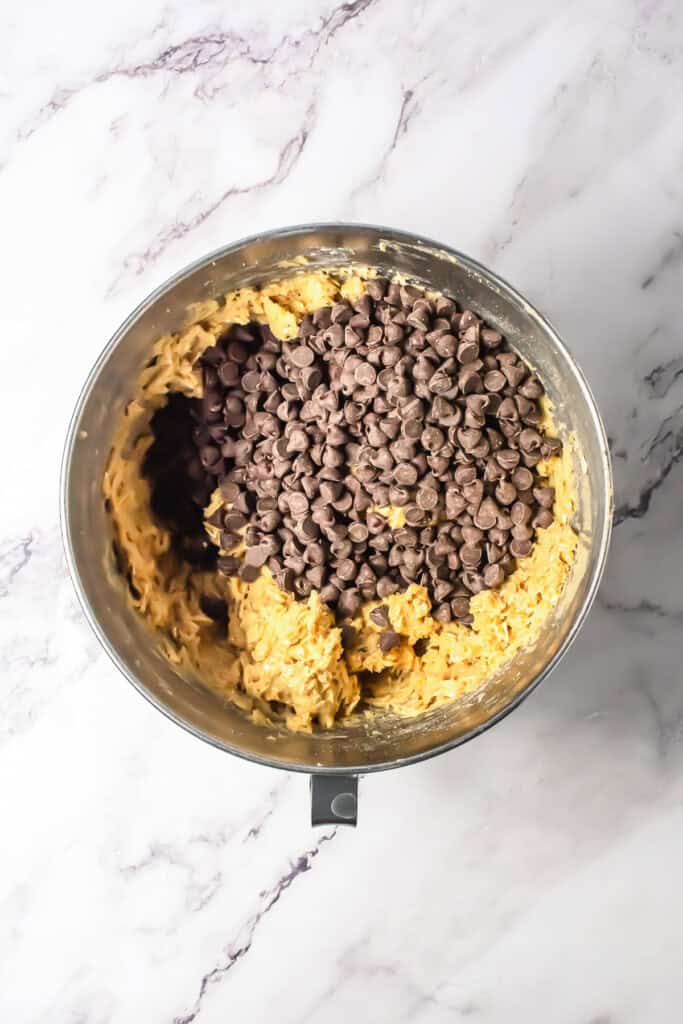 A mixing bowl of oatmeal cookie dough with chocolate chips, perfect for baking chocolate chip bars, sits on a marble countertop.