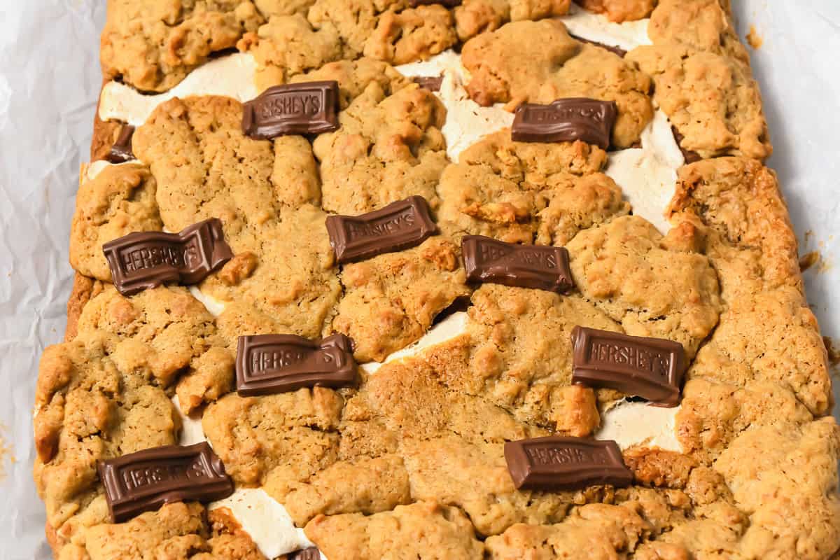 Golden s&rsquo;mores bars topped with melted marshmallow and Hershey&rsquo;s chocolate pieces on a parchment-lined tray&mdash;an irresistible S&rsquo;mores Bars Recipe for any dessert lover.