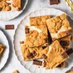 Plates of s'mores bars made from our favorite S’mores Bars Recipe, served with chocolate pieces, graham crackers, and bottles of milk with straws.