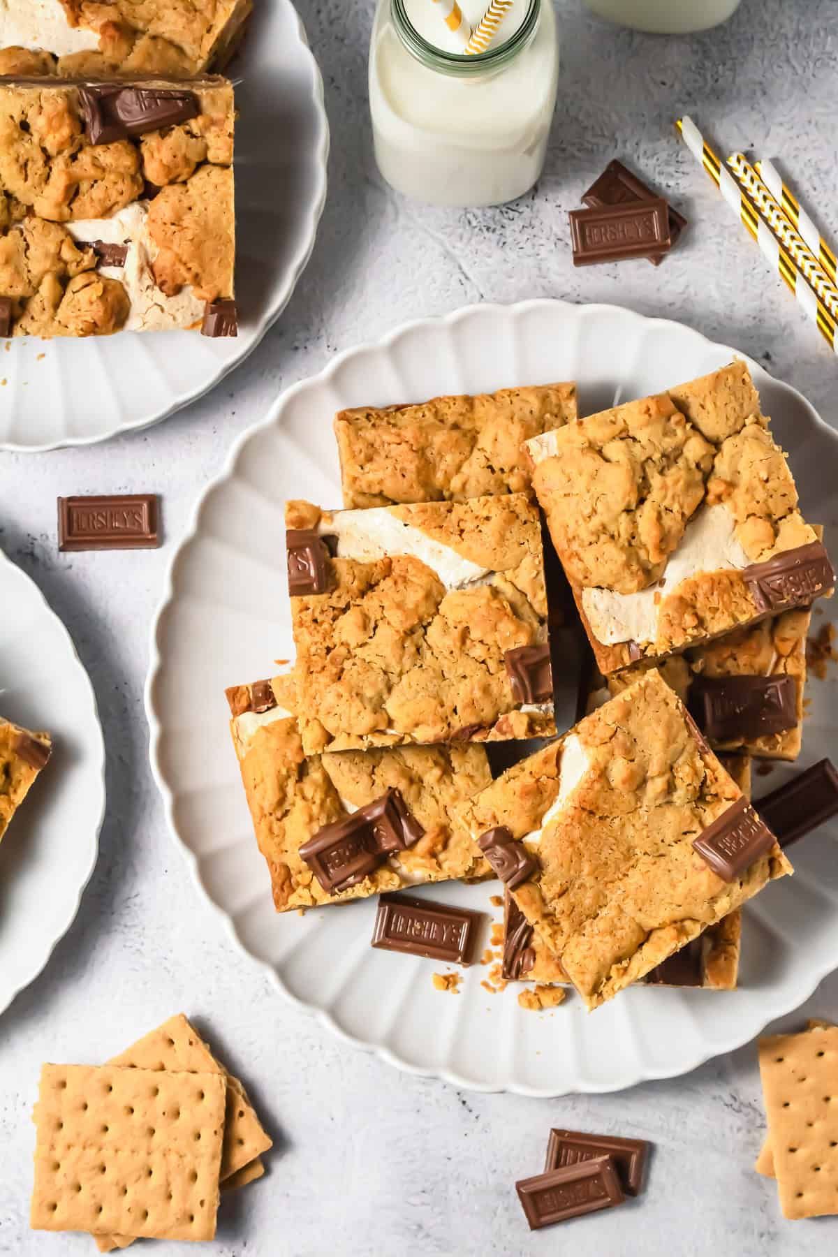 Plates of s'mores bars made from our favorite S&rsquo;mores Bars Recipe, served with chocolate pieces, graham crackers, and bottles of milk with straws.