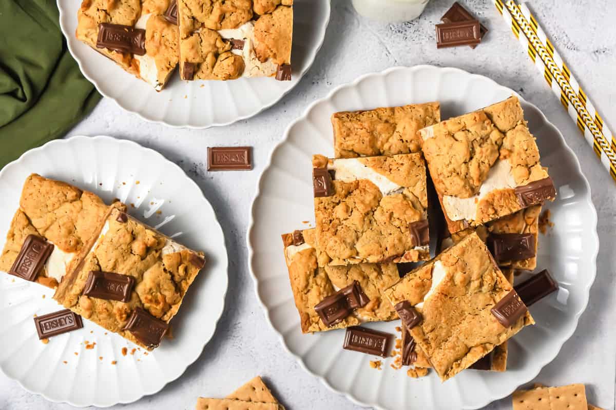 Plates of S&rsquo;mores Bars, made with our irresistible S&rsquo;mores Bars Recipe, are served alongside pieces of chocolate and graham crackers on a light surface&mdash;a must-try dessert recipe for any sweet tooth.