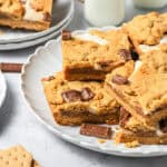 S&rsquo;mores Bars with chocolate pieces on a white plate, served alongside milk bottles and graham crackers&mdash;an irresistible S&rsquo;mores dessert inspired by your favorite campfire treat.