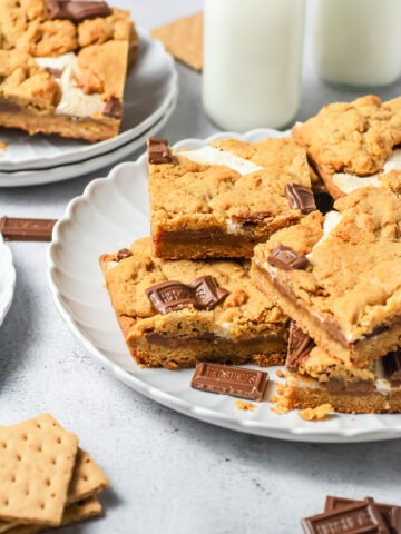 S&rsquo;mores Bars with chocolate pieces on a white plate, served alongside milk bottles and graham crackers&mdash;an irresistible S&rsquo;mores dessert inspired by your favorite campfire treat.