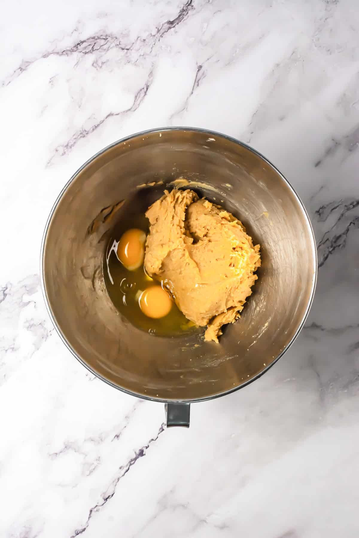 A mixing bowl with cookie dough and two eggs on a white marble countertop, ready to be mixed for a delicious S&rsquo;mores Bars Recipe.