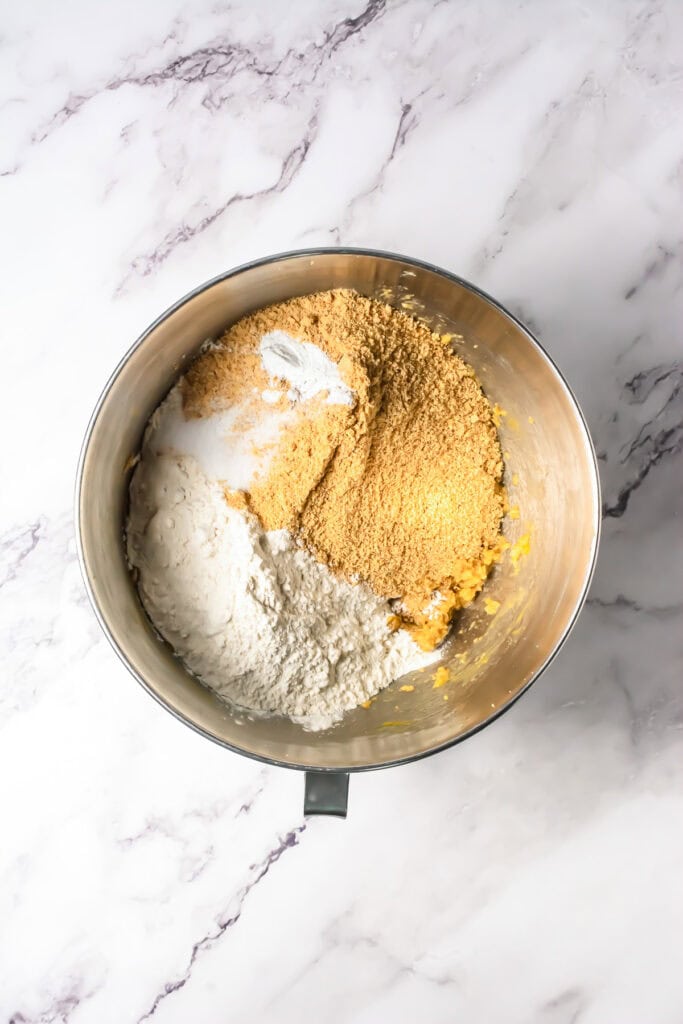 A mixing bowl with flour, graham cracker crumbs, and other baking ingredients on a marble surface, perfect for starting your S&rsquo;mores Bars Recipe.