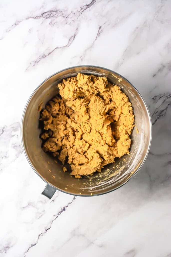 A metal mixing bowl filled with raw cookie dough for a delicious S&rsquo;mores Bars Recipe sits on a white marble surface.