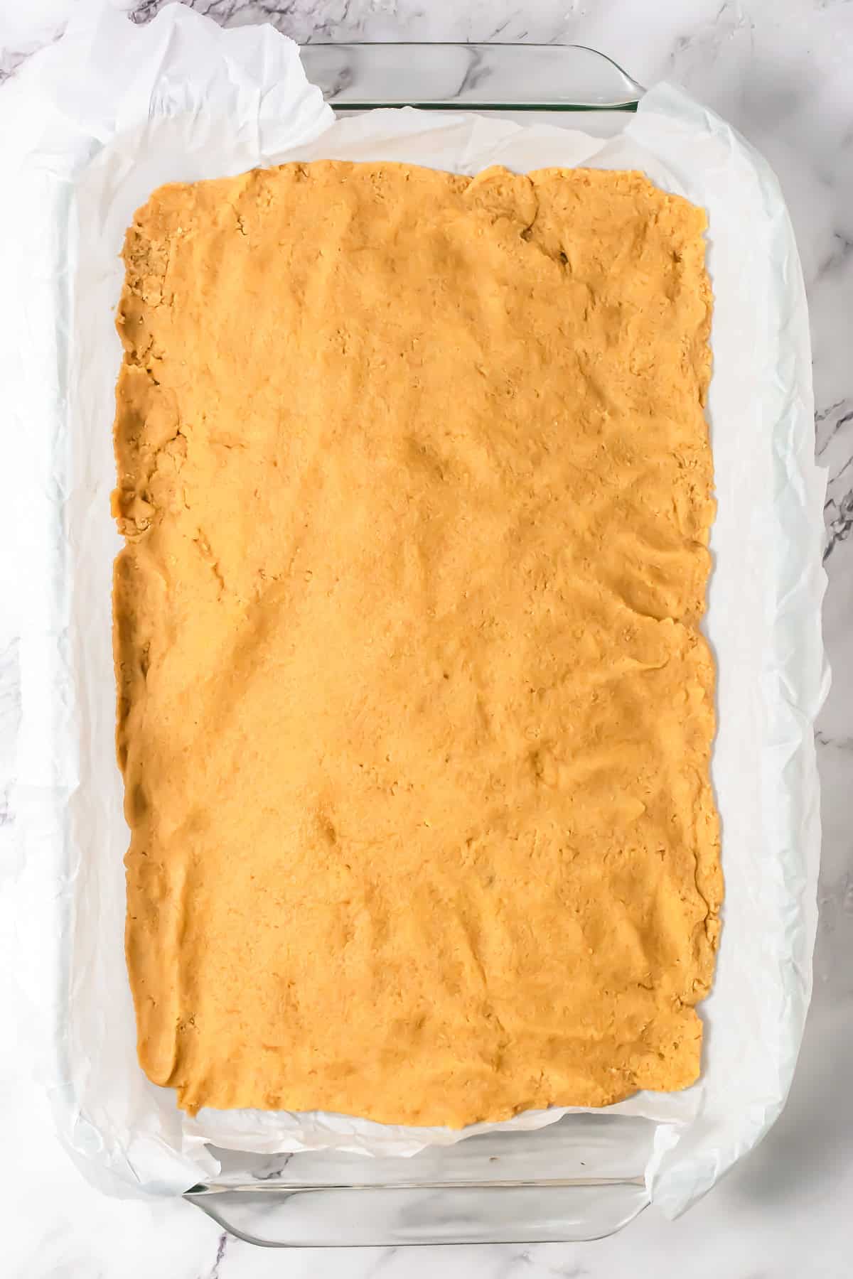 A baking dish lined with parchment paper and filled with an even layer of unbaked dough, perfect for starting your S&rsquo;mores Bars Recipe.