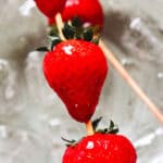 Four fresh strawberries on wooden skewers rest over a glass bowl filled with ice—perfect for making a classic Strawberry Tanghulu or trying out your favorite Tanghulu Recipe at home.