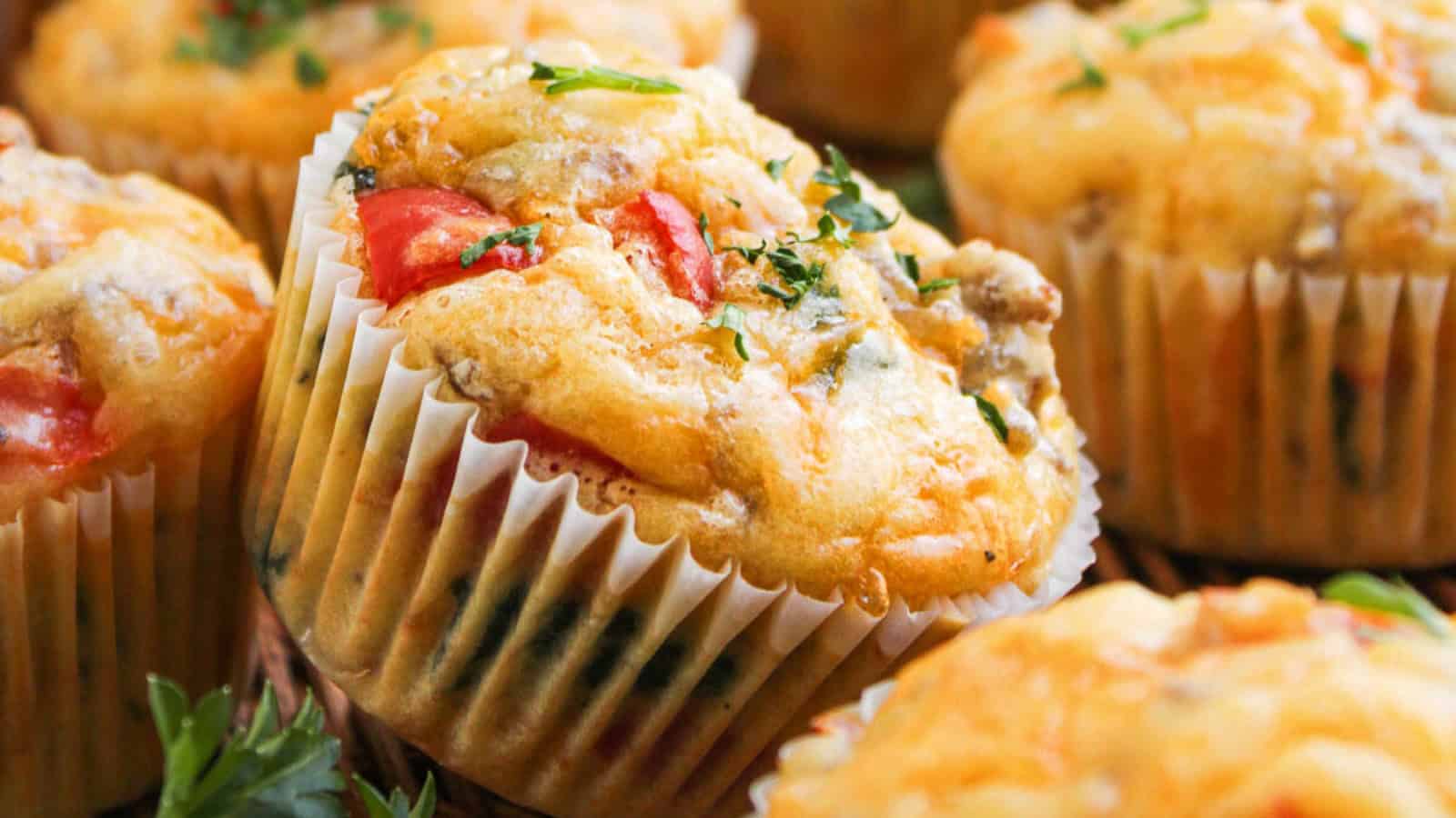 Savory muffins with vegetables and herbs in white paper liners, shown close up.