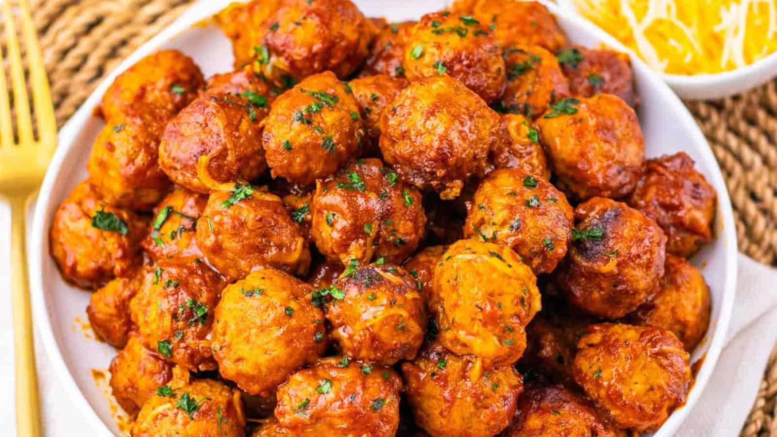 A bowl filled with saucy meatballs garnished with chopped parsley.
