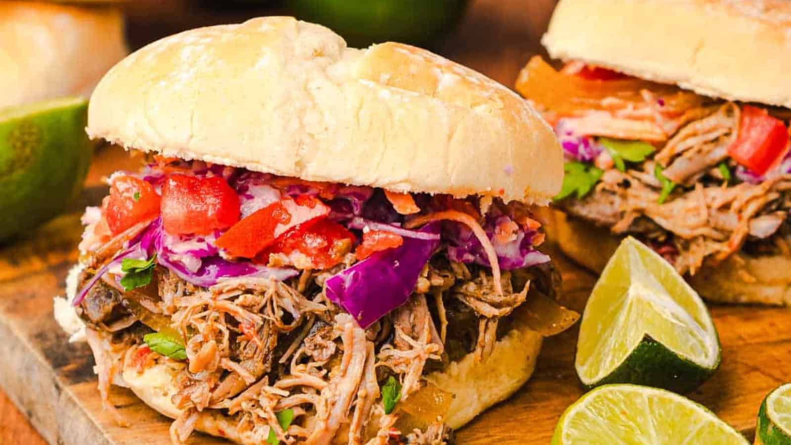 Pulled pork sandwiches with coleslaw and tomato, served with lime halves on a wooden board.
