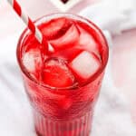 A glass of red Strawberry Acai Refresher with ice and a striped straw, with red ice cubes in a bowl in the background—perfect for a Starbucks copycat experience at home.