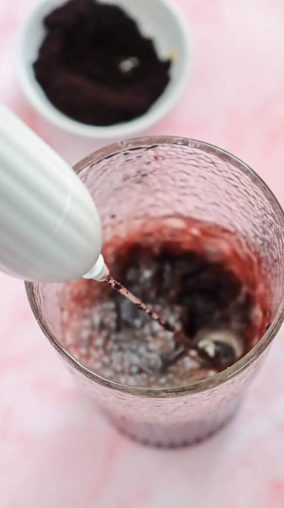 A handheld frother mixing dark powder in a glass, with a bowl of powder in the background&mdash;perfect for making your own Starbucks Copycat Refresher at home.