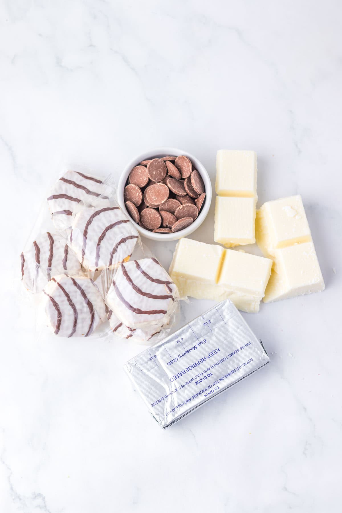 Round chocolate-striped cookies, chocolate wafers, cream cheese, and butter come together to create irresistible Zebra Cake Balls on a white marble surface.