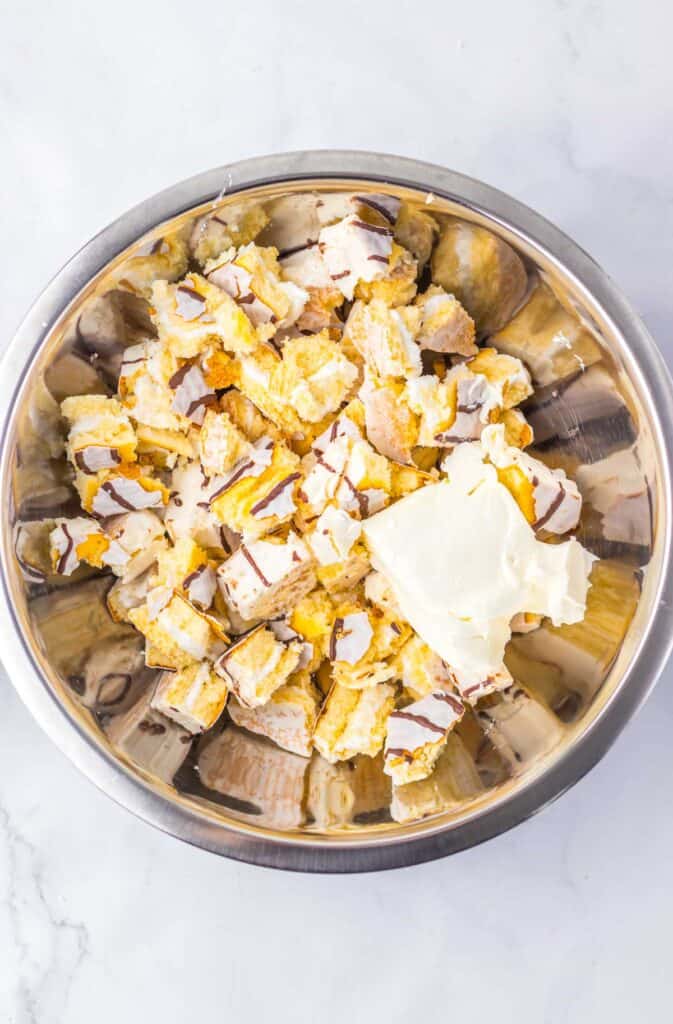 Chopped Zebra Cake Balls and a dollop of cream cheese in a large metal mixing bowl.