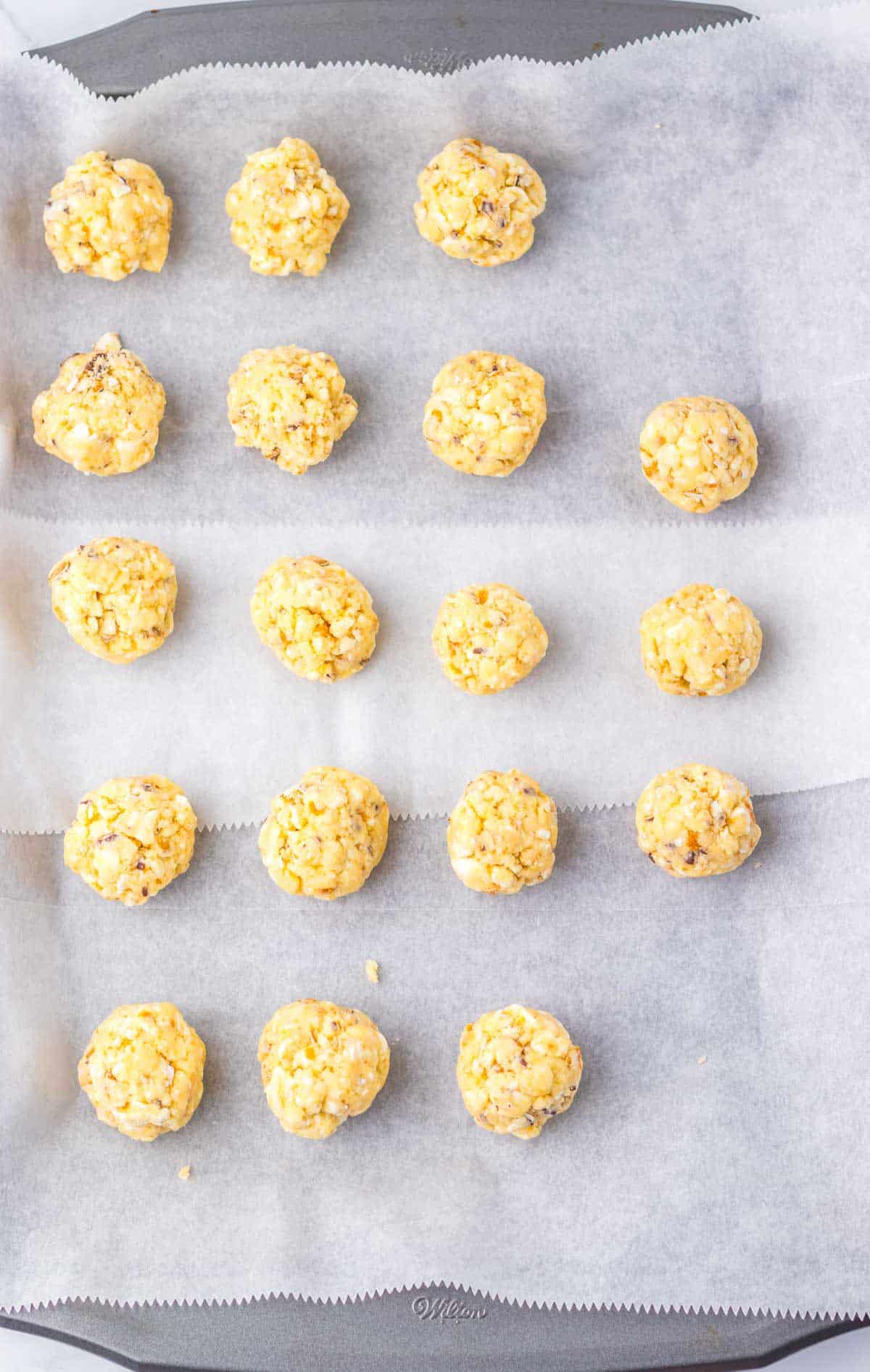 Sixteen popcorn balls arranged in rows on a parchment-lined baking sheet, resembling the playful look of Zebra Cake Balls.